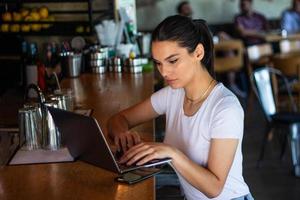 jovem mulher com xícara de café e laptop na cafeteria. mulher fazendo uma pausa. curtindo o trabalho da cafeteria. fazendo negócios na cafeteria foto