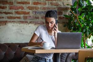 jovem mulher com xícara de café e laptop na cafeteria. mulher fazendo uma pausa. curtindo o trabalho da cafeteria. fazendo negócios na cafeteria foto