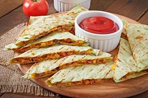 quesadilla mexicano fatiado com legumes e molhos em cima da mesa foto