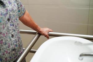 paciente mulher asiática usa trilho de suporte do banheiro no banheiro, barra de segurança do corrimão, segurança no hospital de enfermagem. foto