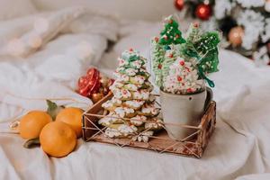 doces de natal, pão de gengibre pintado com glacê, pirulitos e merengues em forma de árvores de natal e tangerinas em uma linda bandeja. bolos caseiros. comida deliciosa para as férias de inverno foto