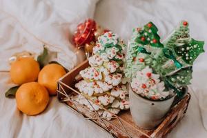 doces de natal, pão de gengibre pintado com glacê, pirulitos e merengues em forma de árvores de natal e tangerinas em uma linda bandeja. bolos caseiros. comida deliciosa para as férias de inverno foto