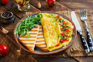 omelete frito com tomate, cebola e ervas. delicioso café da manhã com ovos e torradas foto