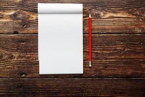 bloco de notas com lápis vermelho em um fundo de mesa de madeira marrom, para educação, escreva objetivos e ações foto