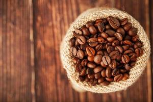 grãos de café em um saco de serapilheira em um fundo de madeira. foto