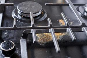 cozinha suja suja fogão preto após a sopa ferver, manchas de comida seca, manchas de gordura sobras de comida seca foto