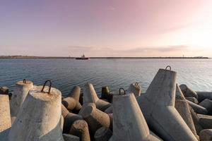 rebocador navegando no mar para rebocar o navio para o porto. quebra-mares tetrápodes no porto. belo pôr do sol sobre o cais. foto