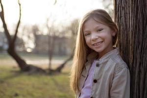 menina sorridente ao lado de uma árvore foto