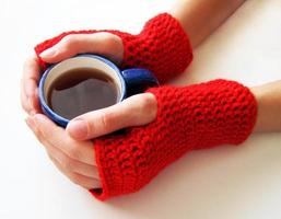 mãos femininas em luvas vermelhas estão segurando um copo de bebida quente. mulher segura uma xícara de café foto