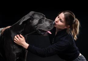 jovem mulher bonita posa com seu animal de estimação, um dogue alemão, destacado em um fundo preto. foto