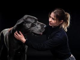 jovem mulher bonita posa com seu animal de estimação, um dogue alemão, destacado em um fundo preto. foto