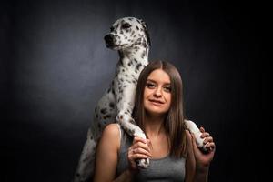 uma jovem bonita está brincando com seu animal de estimação dálmata, isolado em um fundo preto. foto