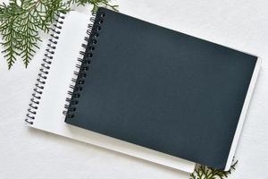 caderno de desenho preto e branco em uma mola deitado sobre uma toalha de mesa de linho com raminhos de thuja verde foto