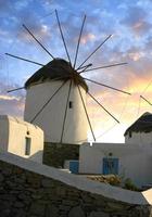 moinho de vento na ilha grega de mykonos com o pôr do sol iluminando as nuvens. foto