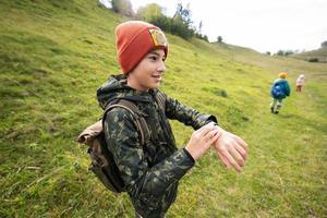 menino com mochila olhando para seus relógios inteligentes durante uma caminhada. foto