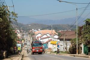 luang prabang, laos - 23 de janeiro de 2018. vista na rua movimentada com transporte diferente, edifícios residenciais, turistas e população local e com montanhas no fundo. foto