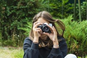 linda garota adolescente com uma câmera, uma garota tirando fotos em uma câmera vintage retrô na grama do parque, um conceito de hobby