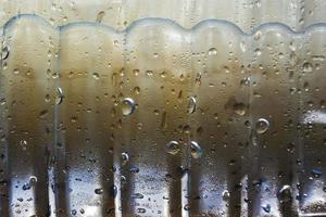 gotas de condensado drenam de uma garrafa fria de água potável em um dia quente, fundo abstrato com água e gotas foto