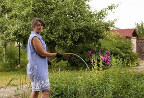 mulher jovem e bonita regando flores no jardim com uma mangueira de borracha, país se preocupa foto