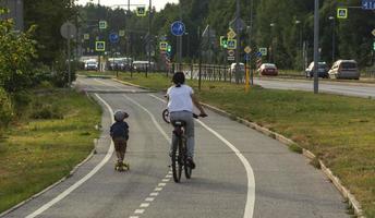 mãe e filho andam de bicicleta e scooter em uma ciclovia na cidade, passeio de bicicleta em família, recreação ativa, vida na cidade foto