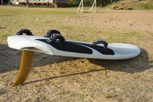 prancha de surf fica na areia da praia na margem do lago, mar, esportes aquáticos, estilo de vida ativo, férias, calor, descanso foto