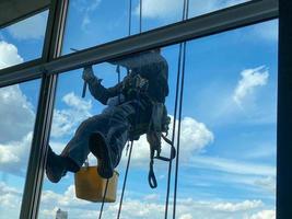 alpinista industrial pendurado no varal e lava janelas, edifício moderno de fachada de vidro foto