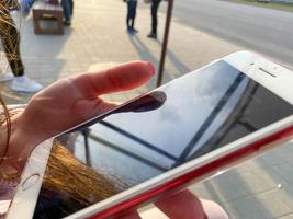 linda menina mulher sentada e segurando um smartphone de celular branco moderno na mão com os dedos com uma bela manicure na rua foto