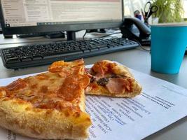 deliciosa nutritiva linda pizza apetitosa com linguiça piperone fica em uma área de trabalho de negócios em frente a um computador no escritório. um almoço rápido para um trabalhador de escritório foto