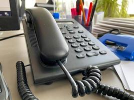 telefone fixo preto com tubo, botões e fio na mesa de trabalho na mesa do escritório com material de escritório. trabalho de negócios foto