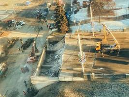 construção de um novo viaduto no centro da cidade. guindastes de construção altos e amarelos estão construindo uma ponte de vigas pesadas. perto de semáforos e tráfego intenso foto