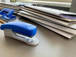 um grande grampeador azul para grampear papel fica ao lado das pastas de documentos na mesa de trabalho do escritório. papelaria foto