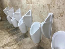 o banheiro do homem com linha de mictórios de cerâmica branca moderna em banheiro público ou restaurante ou hotel ou shopping, design de interiores foto