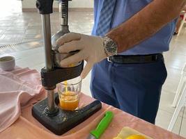 o processo de fazer suco de laranja amarelo espremido na hora, um homem espreme o suco em um copo com as mãos em um hotel em um resort paradisíaco do sul do país tropical oriental quente foto