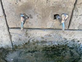 três torneiras de onde sai água. a água é limpa e clara para beber. guindastes feitos em uma parede de pedra