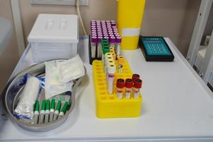 diagnósticos laboratoriais. tubos de ensaio com tampas multicoloridas estão no suporte. próximo a ele está um vaso médico com agulhas e material de transferência, torniquetes para uma veia. tomando sangue venoso foto