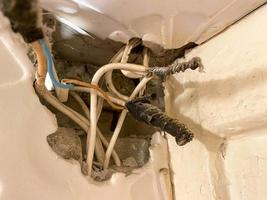 velhos fios torcidos emaranhados em teias de aranha e poeira em um buraco em uma parede em um canteiro de obras. eletricista industrial muito ruim foto