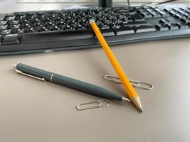 caneta esferográfica verde automática e lápis de escrita na mesa de escritório com teclado de computador. trabalho de negócios foto