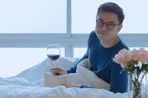 uma pessoa sorridente que lê o livro na cama com um copo de vinho tinto. bom conceito de saúde mental. foto