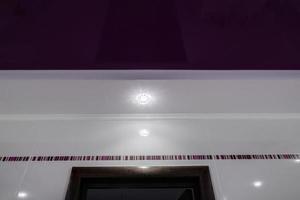 detalhe do teto de canto com intrincado trabalho de estuque. teto falso e drywall com lâmpadas halógenas em sala em apartamento ou casa. esticar teto roxo de forma complexa. foto