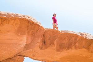 garota turista fica na famosa ponte de arco em pose de deserto de wadi rum e aprecia a vista panorâmica de formações rochosas cênicas foto