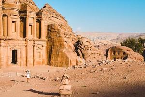 turista de mulher caucasiana em vestido branco segura sua pose de chapéu branco em ad deir ou el deir, o monumento esculpido na rocha na antiga cidade de petra, na jordânia. patrimônio mundial da unesco foto