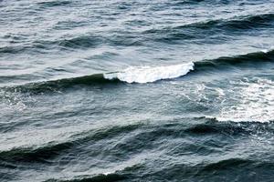 águas do mar azul profundo espirrando com ondas espumosas, superfície da água do oceano ondulada azul escuro, copie o espaço foto