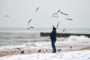 velho alimentando pássaros no mar no inverno foto