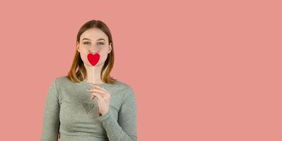 retrato de estúdio de São Valentim segurando o coração. mulher loira sorridente com corações contra fundo rosa banner copyspace foto