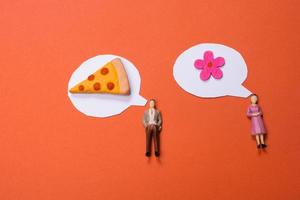 estatueta de homem e mulher, flor falsa, pedaço de pizza e mini balões de fala recortados em papel