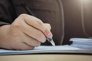 feche a mão do empresário assinando documento com caneta. conceitos de negócios em contratos de investimento, acordos e aprovações, mou. foto