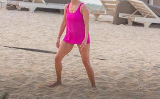 jovem mulher com camisa rosa jogando vôlei de praia praia foto