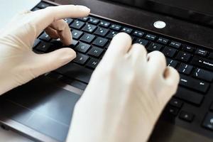 mãos em luvas digitando no teclado do laptop. conceito de proteção contra vírus foto