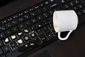 derramar café da xícara branca no teclado do computador portátil foto