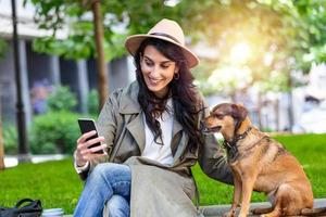 retrato de garota satisfeita abraçando cachorro engraçado e tirando uma selfie com seu celular. mulher jovem sorridente na camisa branca, aproveitando o bom dia e posando com animal de estimação foto